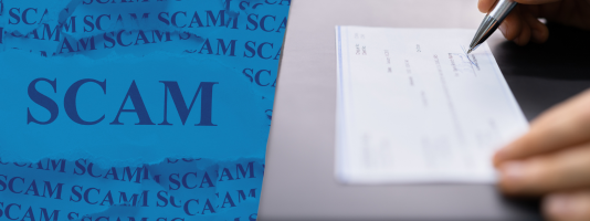 Image of someone signing a check over the word, "scam" in all caps. 